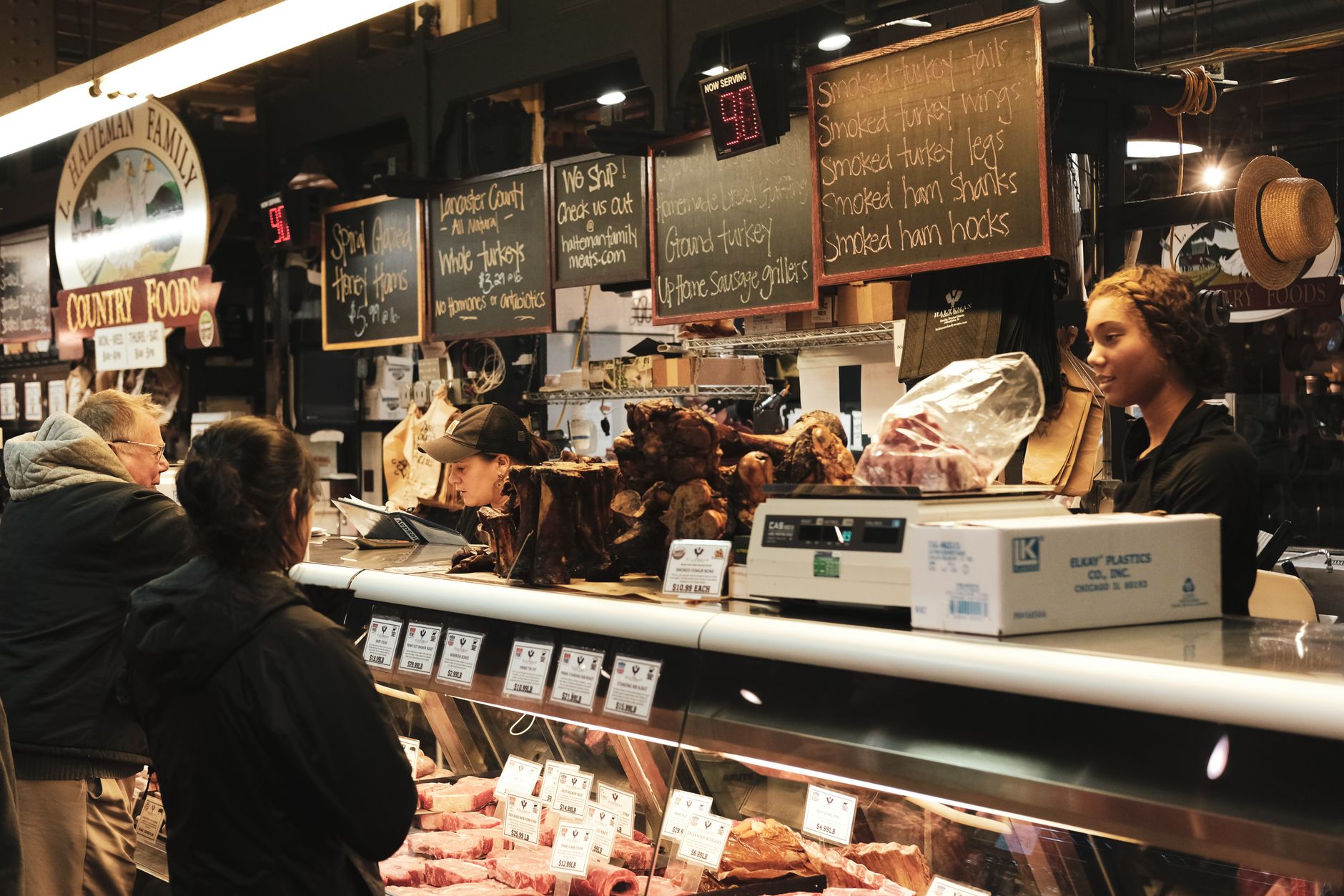 A deli counter with assorted meats and staff serving customers.